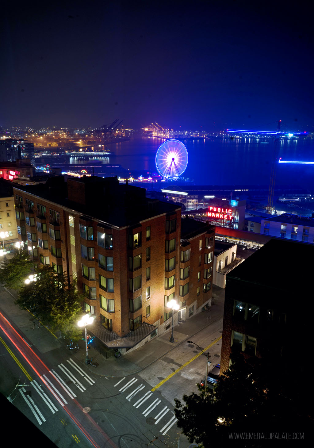 Seattle waterfront at night with the glowing lights of the Pike Place Market sign and Seattle Wheel