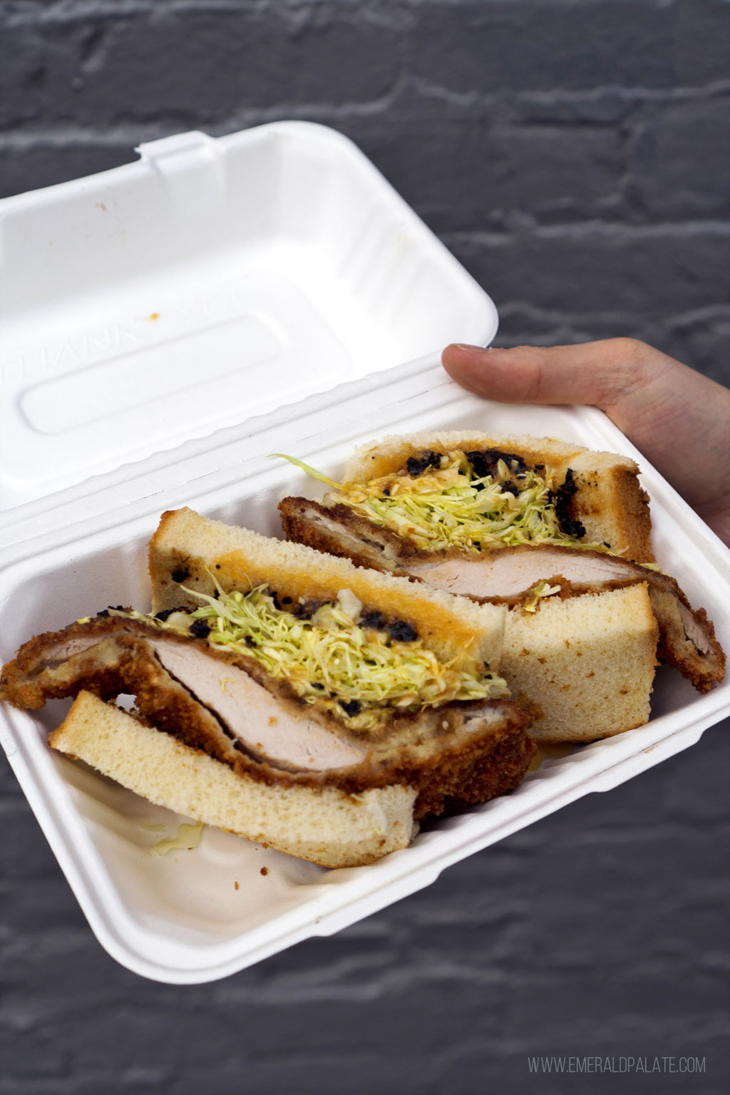 person holding a takeout container of a messy katsu sando