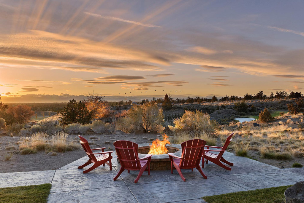 Adirondack chairs around a fire pit overlooking the landscape at sunset
