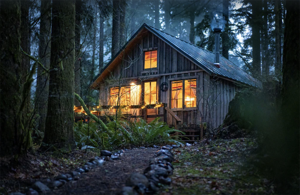 a cabin glowing with lights through the window at dusk