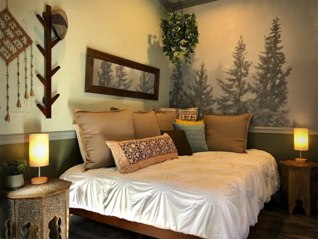 a bed in a cottage with a mural that has evergreen trees on the wall