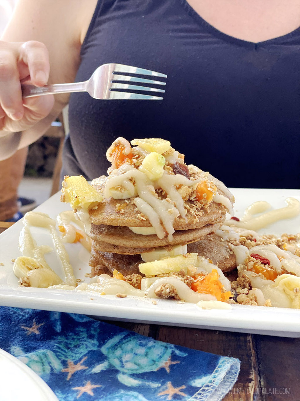person diving fork into stack of pancakes covered with fruit and cream