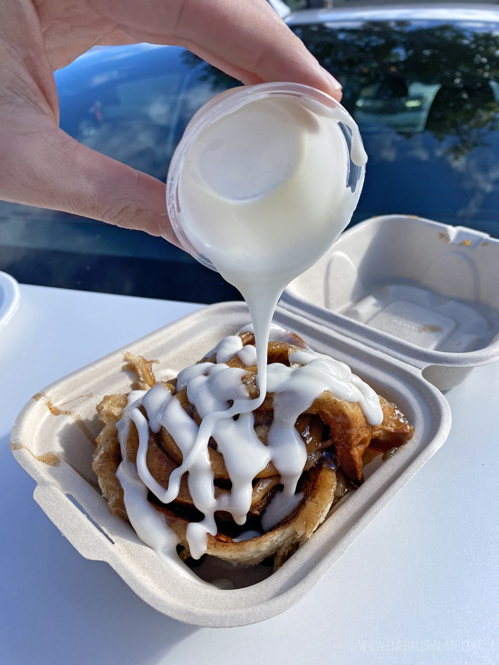 person pouring icing on a gooey cinnamon roll