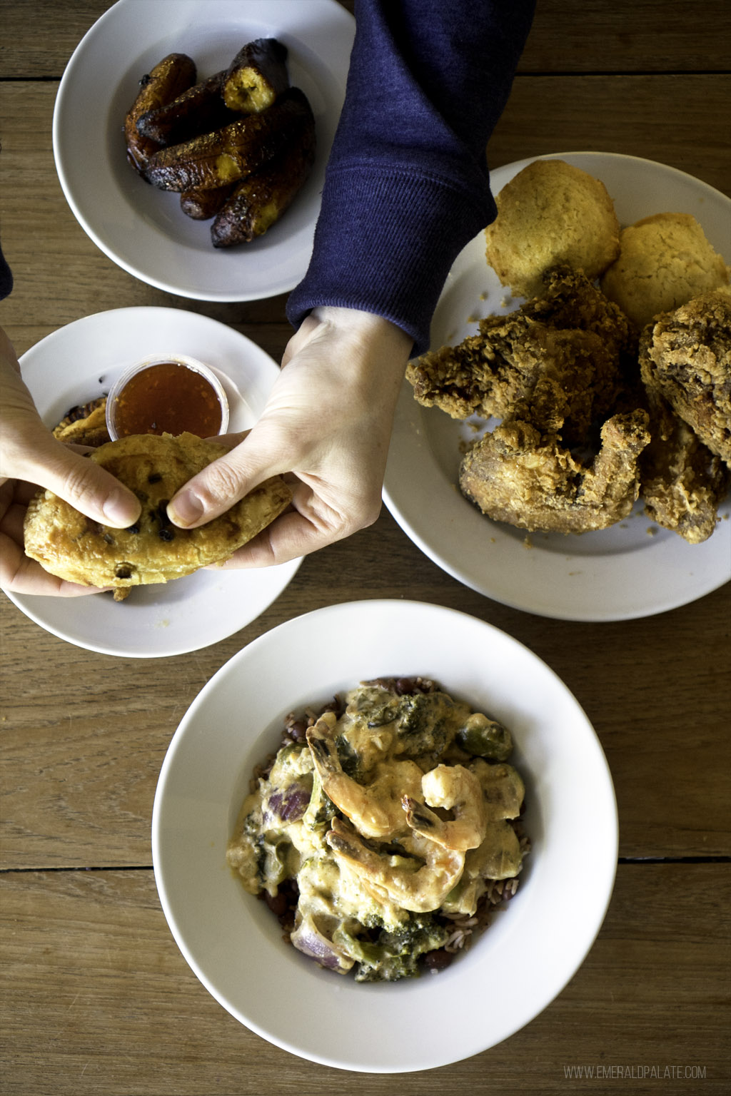 overshot head of a table with Caribbean food and person breaking empanada