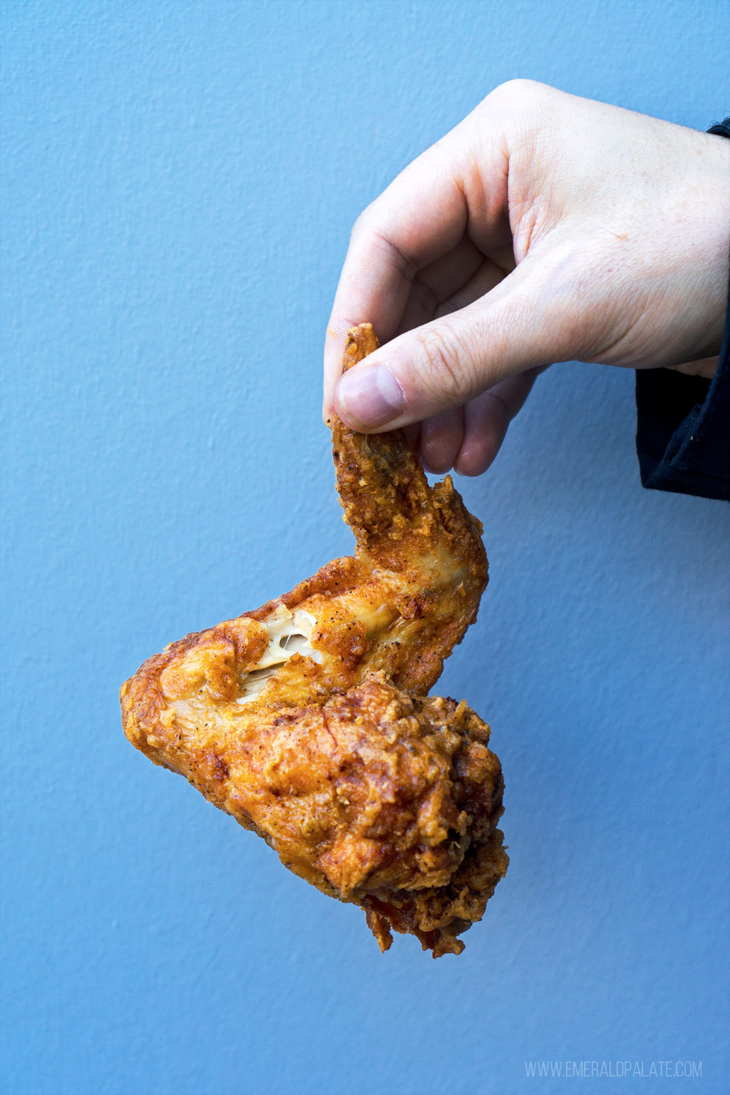 person holding a fried chicken wing from a place that's a hidden gem in Seattle