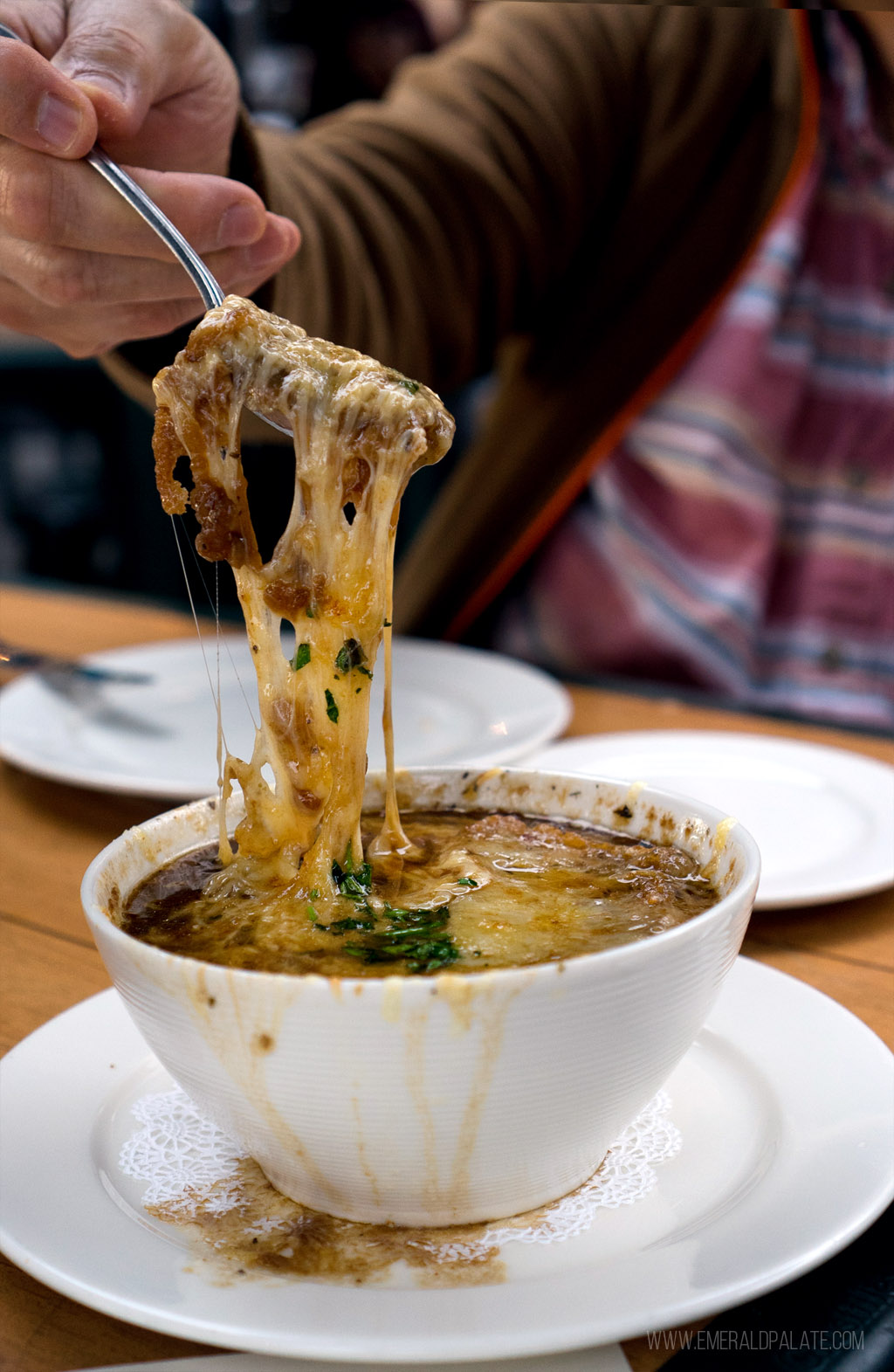 person pulling stringy cheese with a spoon out of French onion soup