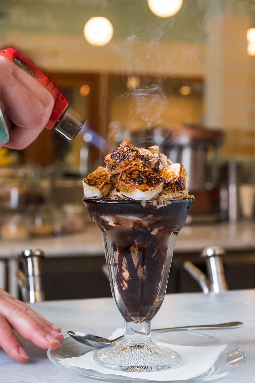 person bruleeing marshmallow on top of a sundae