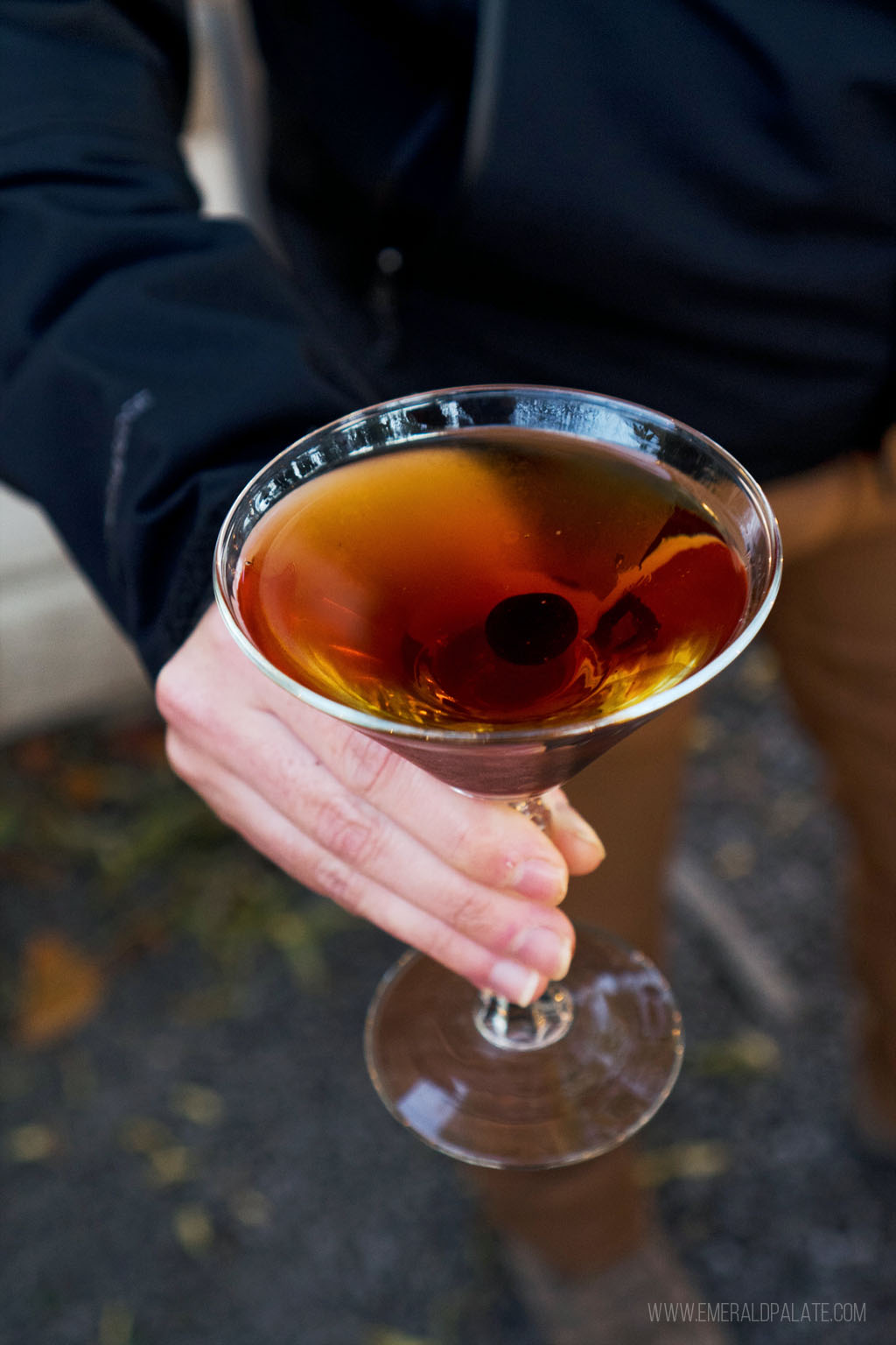 person holding a martini glass with a cherry and cocktail in it