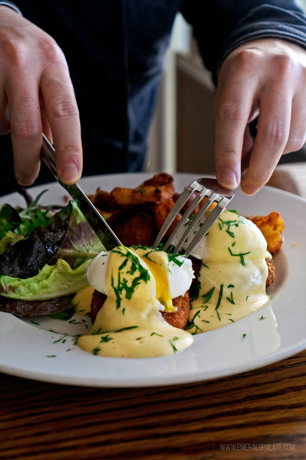 person cutting into an eggs Benedict with yolk running