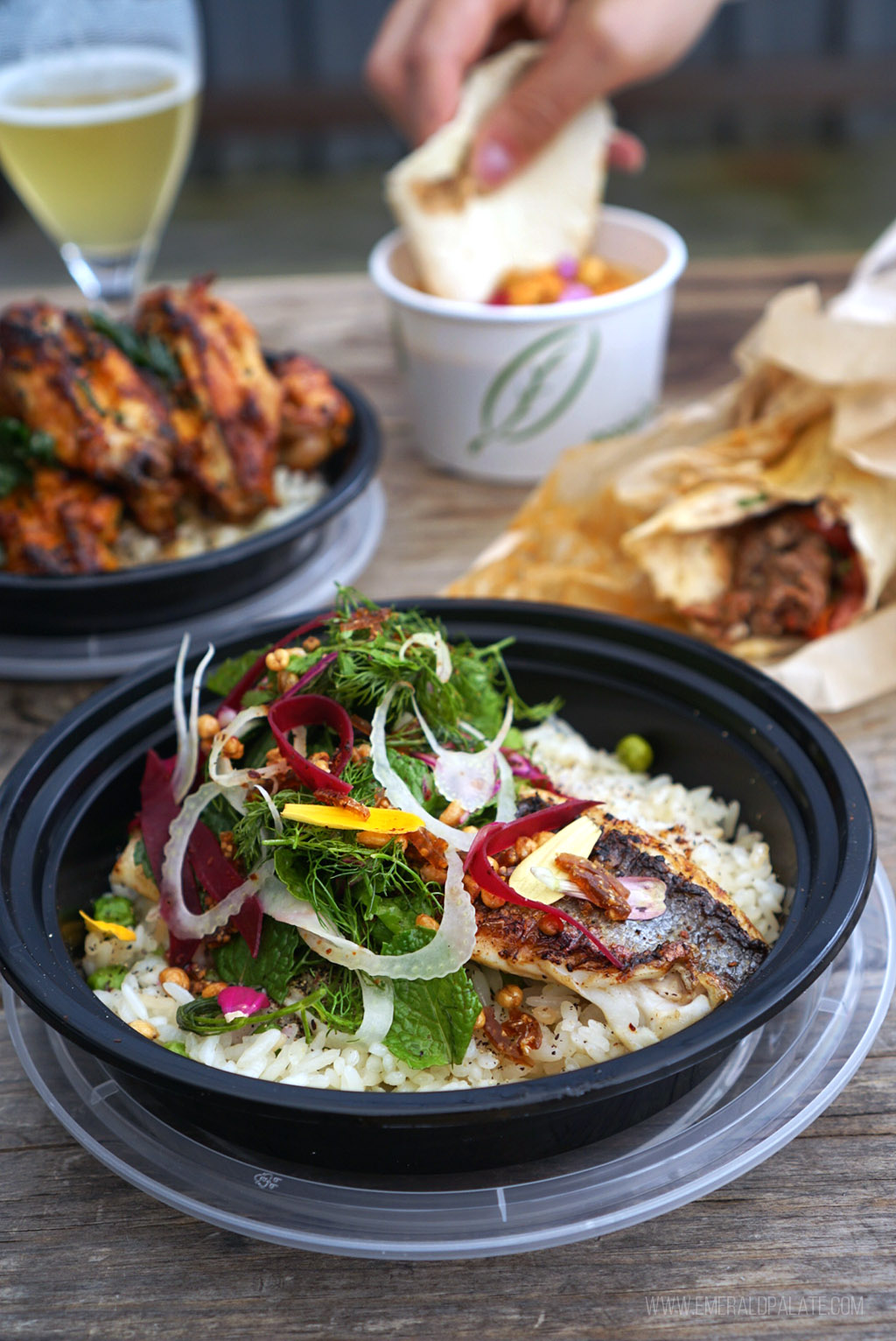 table full of Mediterranean food in Seattle, including fish heaping with herbs, chicken wings, lamb kebabs, hummus, and beer