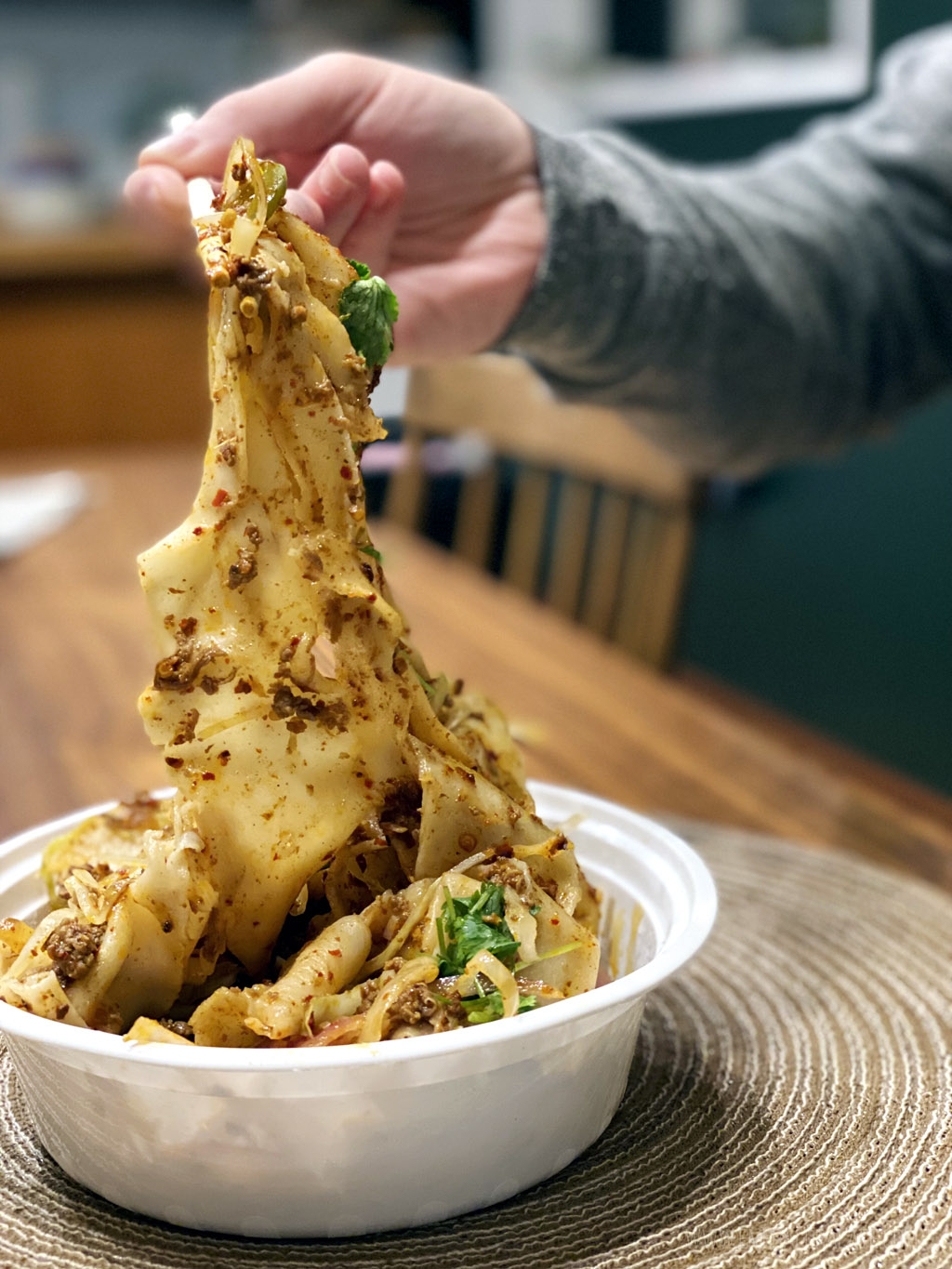 person pulling hand shaven noodles with chopsticks from one of the best takeout restaurants in Seattle