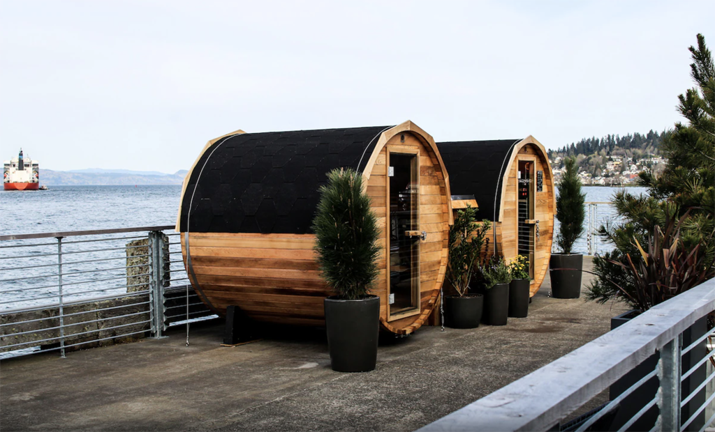 2 barrel saunas on a dock overlooking the water with a ferry in the background