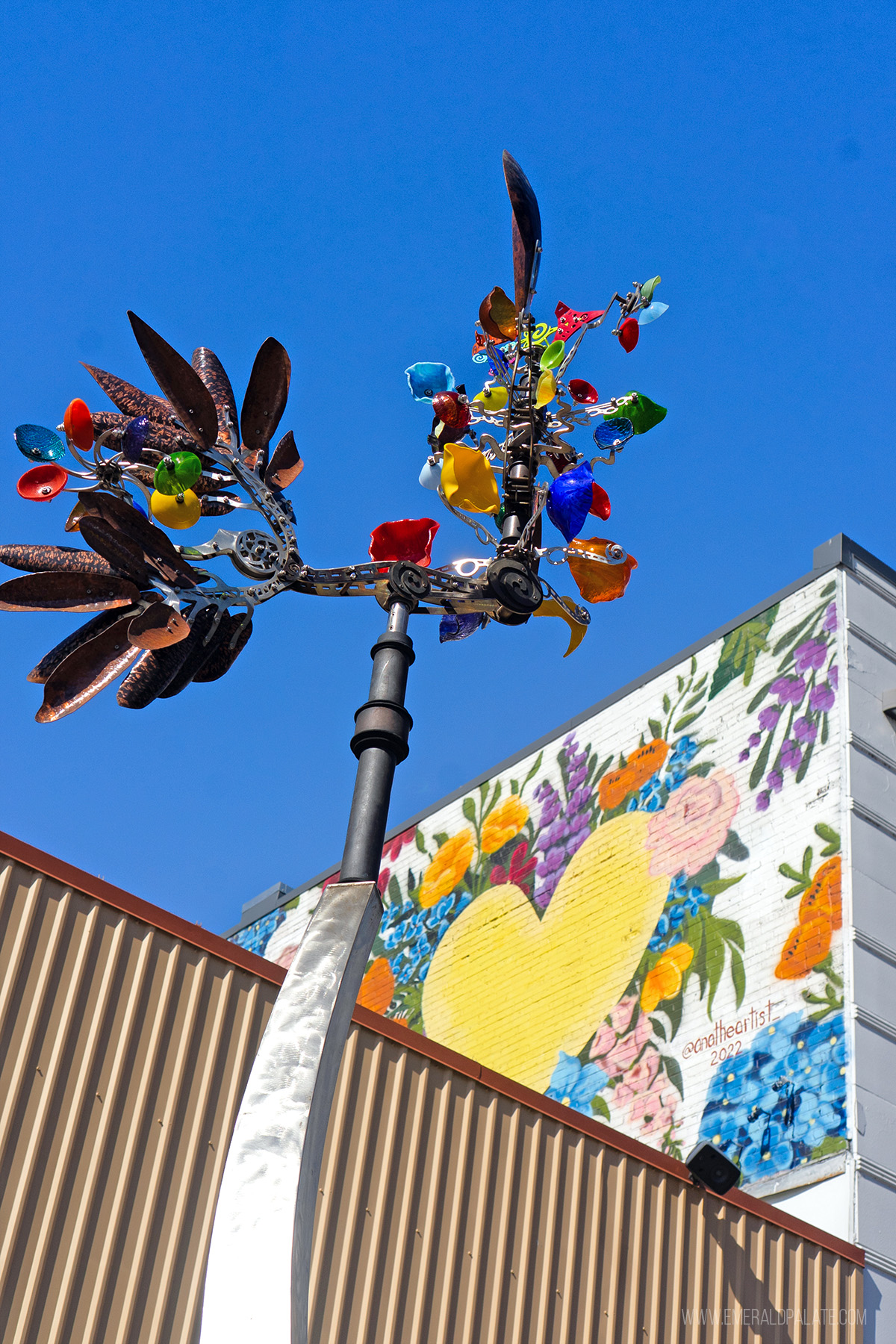 funky weathervane art structure in front of a mural