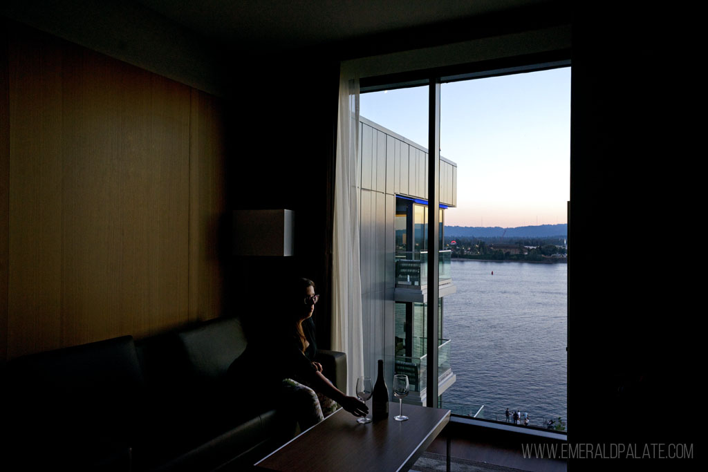 woman enjoying wine in a hotel room overlooking a river at sunset