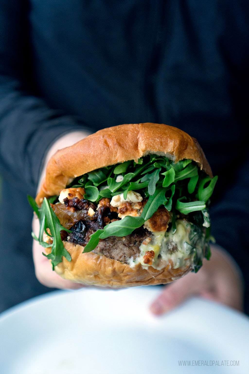 close up of a messy lamb burger with arugula, cheese, onions, and sauce