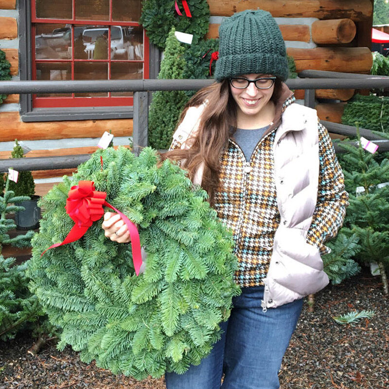 woman carrying a Christmas wreath while enjoying on the of the best Seattle Christmas activities