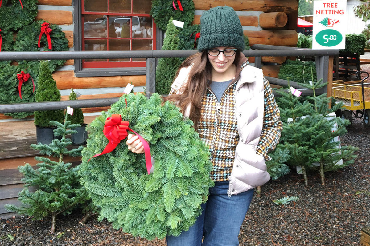 woman carrying a Christmas wreath while enjoying on the of the best Seattle Christmas activities