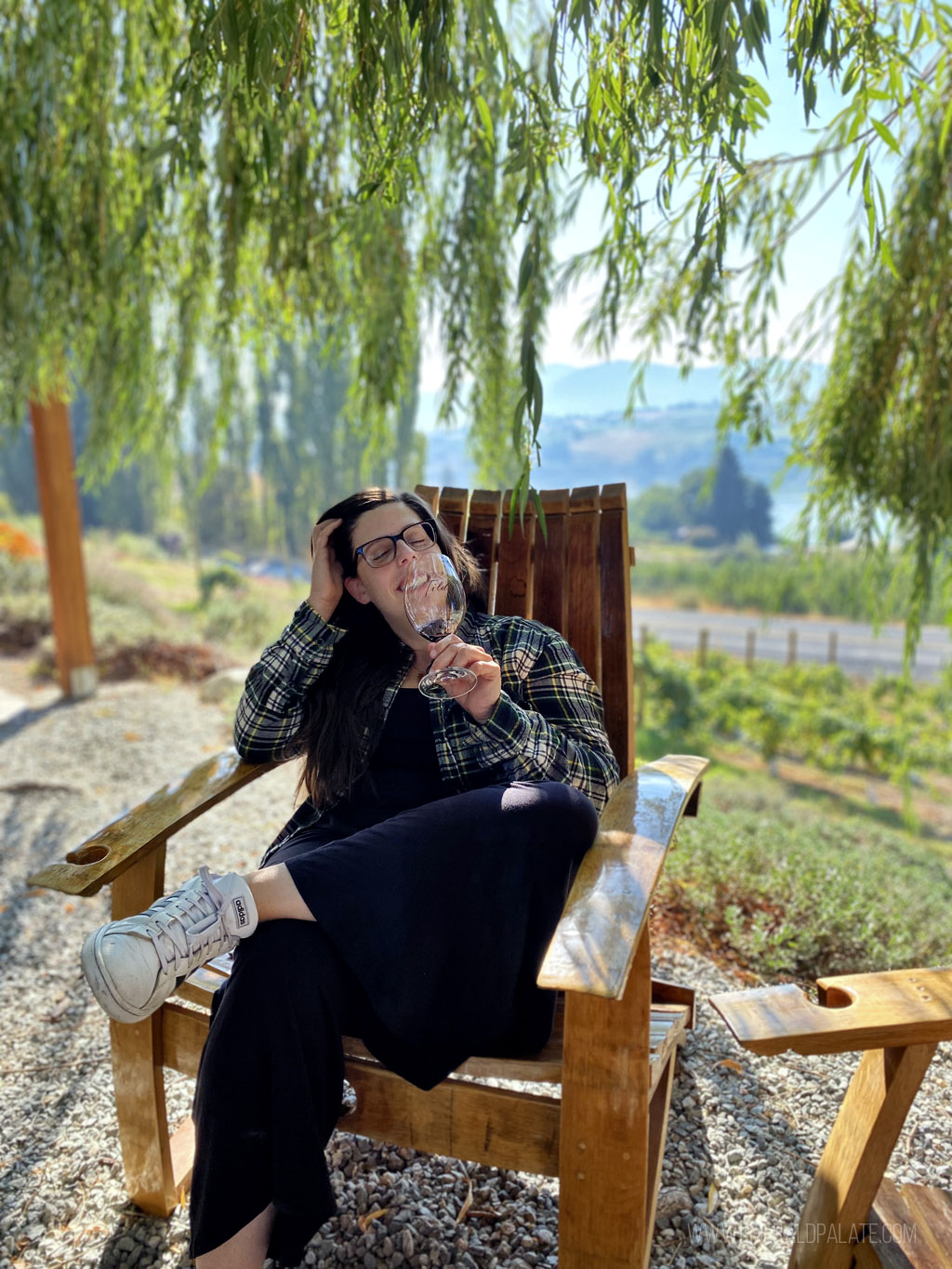 woman drinking wine on an Adirondack chair under a willow tree in Lake Chelan
