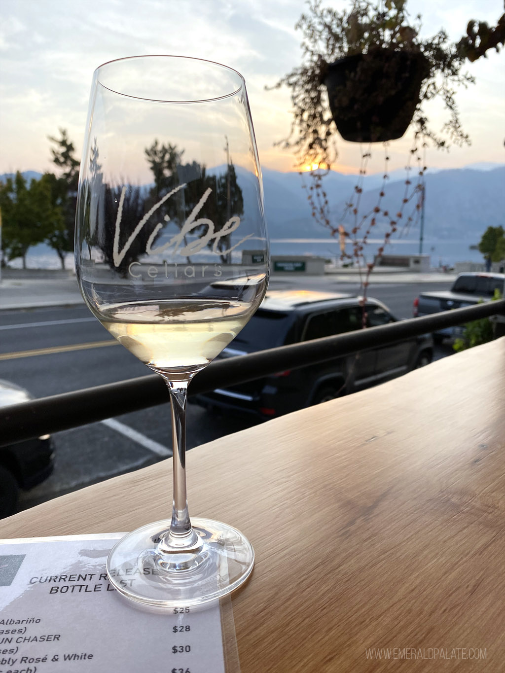 glass of white wine with Vibe Cellars logo and Manson Lake at sunset in the background