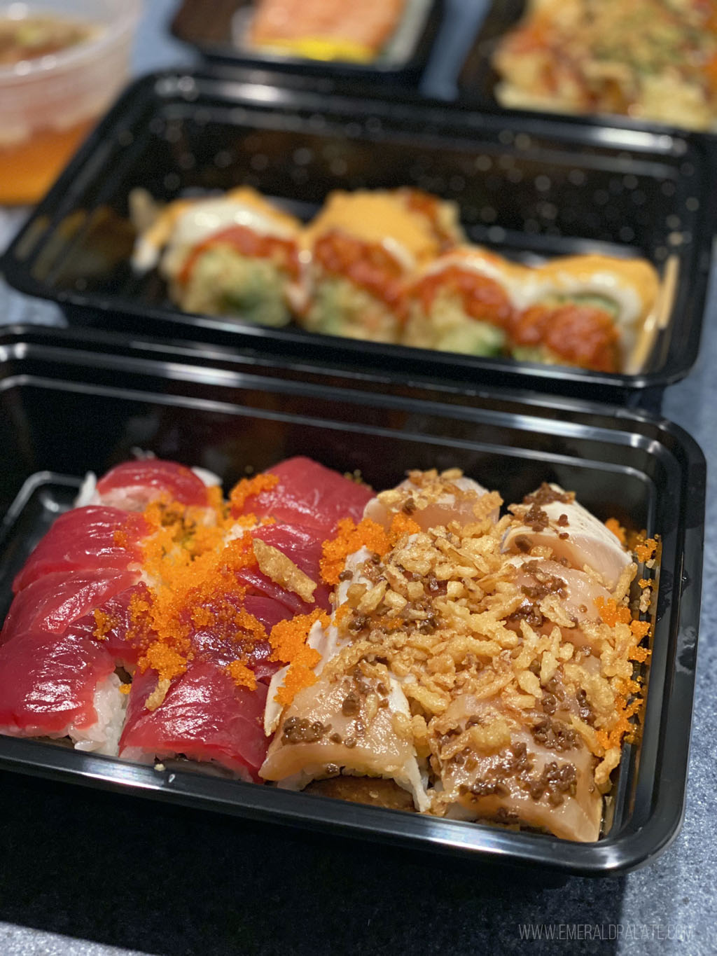 sushi rolls covered in sauces and crunchies in a takeout container