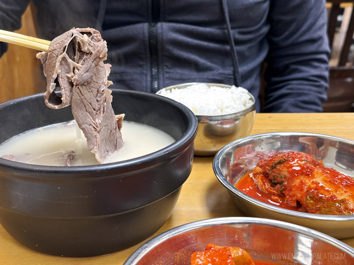 person picking up oxtail from a bowl of Korean soup