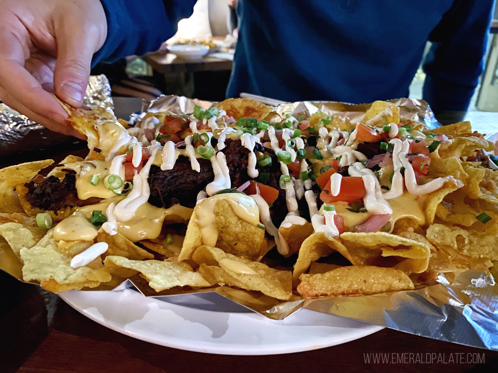 person picking up a nacho from a messy nacho plate