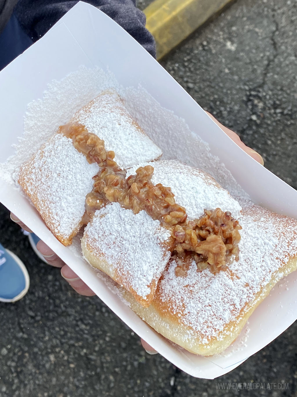 person holding a takeout container of beignets covered with pralines