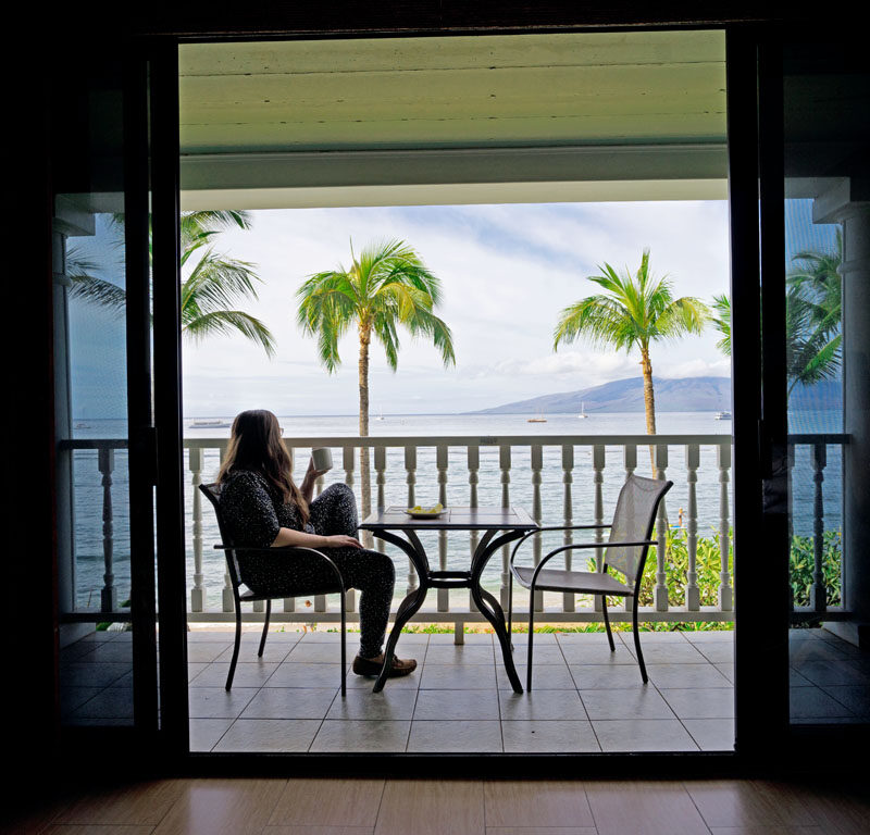 a woman pondering where to stay in Maui while looking out at the ocean with coffee in a Maui hotel