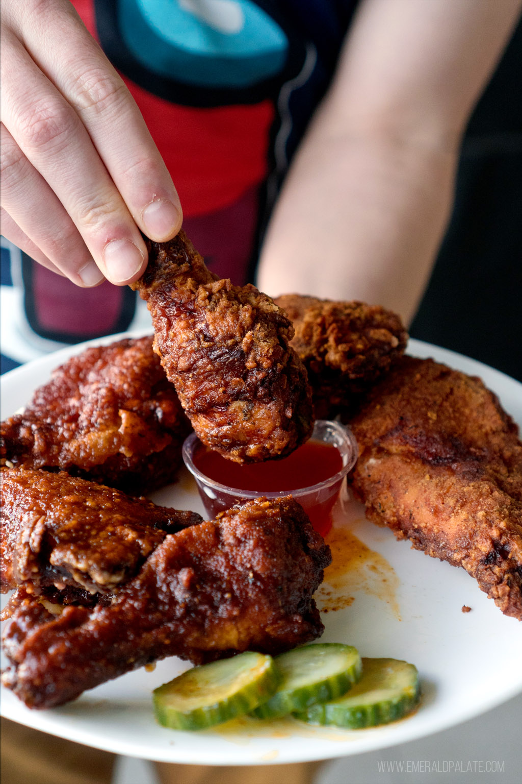 person dipping the best fried chicken in Seattle drumstick into spicy honey