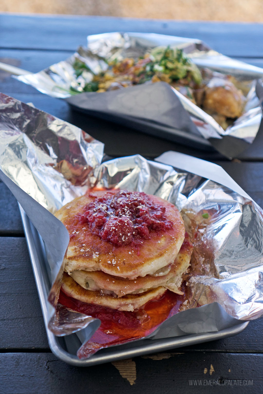 pancakes topped with berries in a takeout container with tinfoil