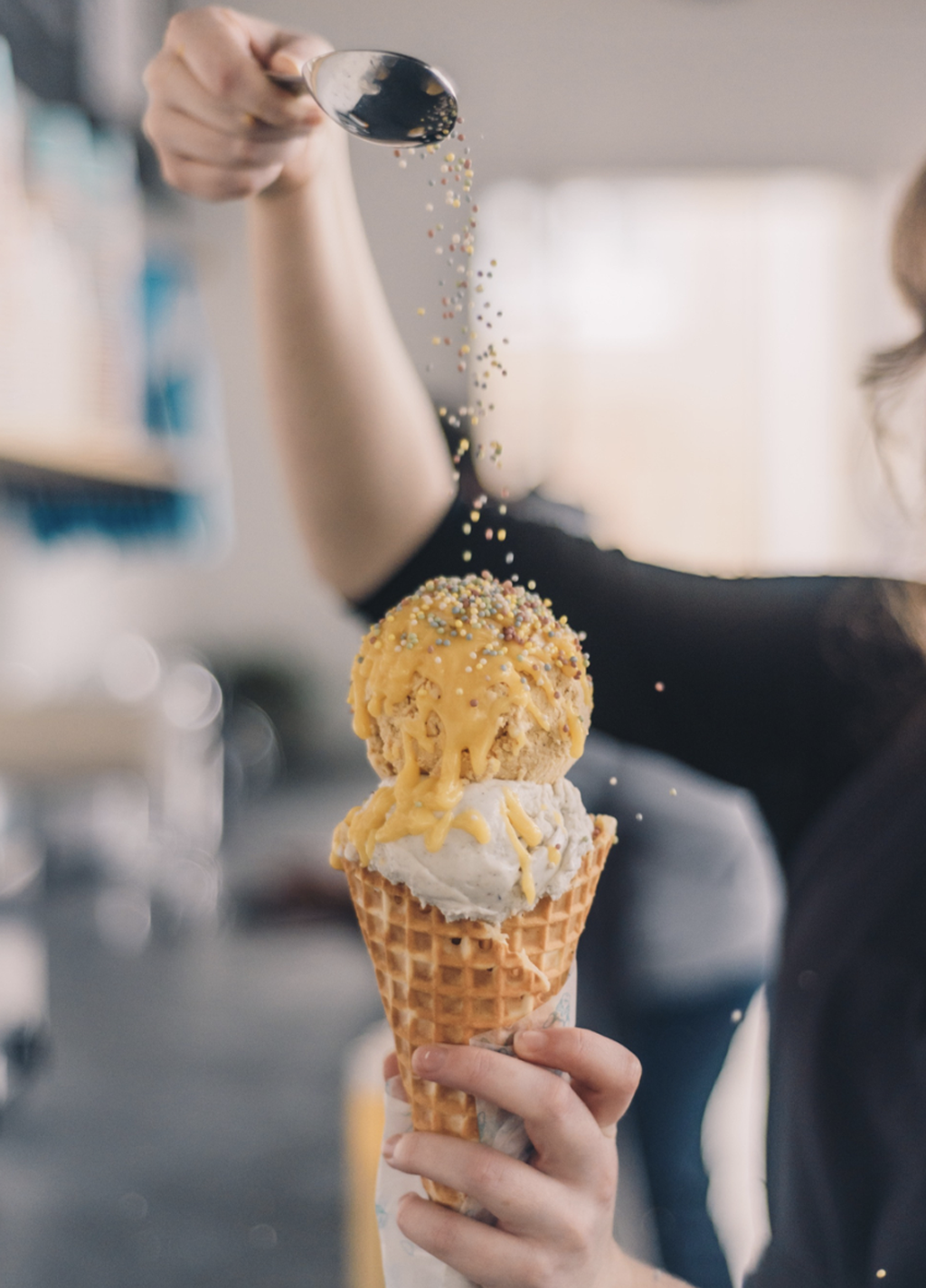 person spooning nuts over a double scoop ice cream waffle cone