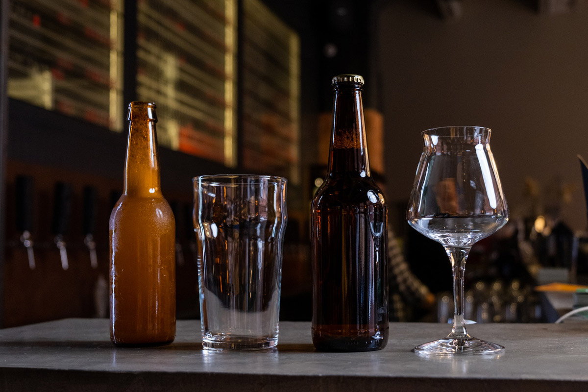 bottles of craft beer and glasses lined up on a bar top