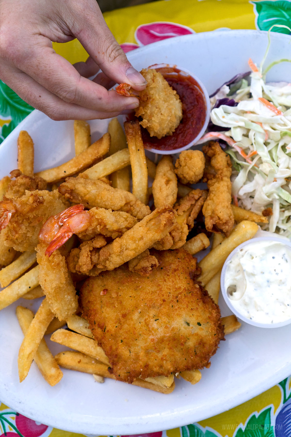 person dipping fried shrimp into cocktail sauce on a place of fish and chips