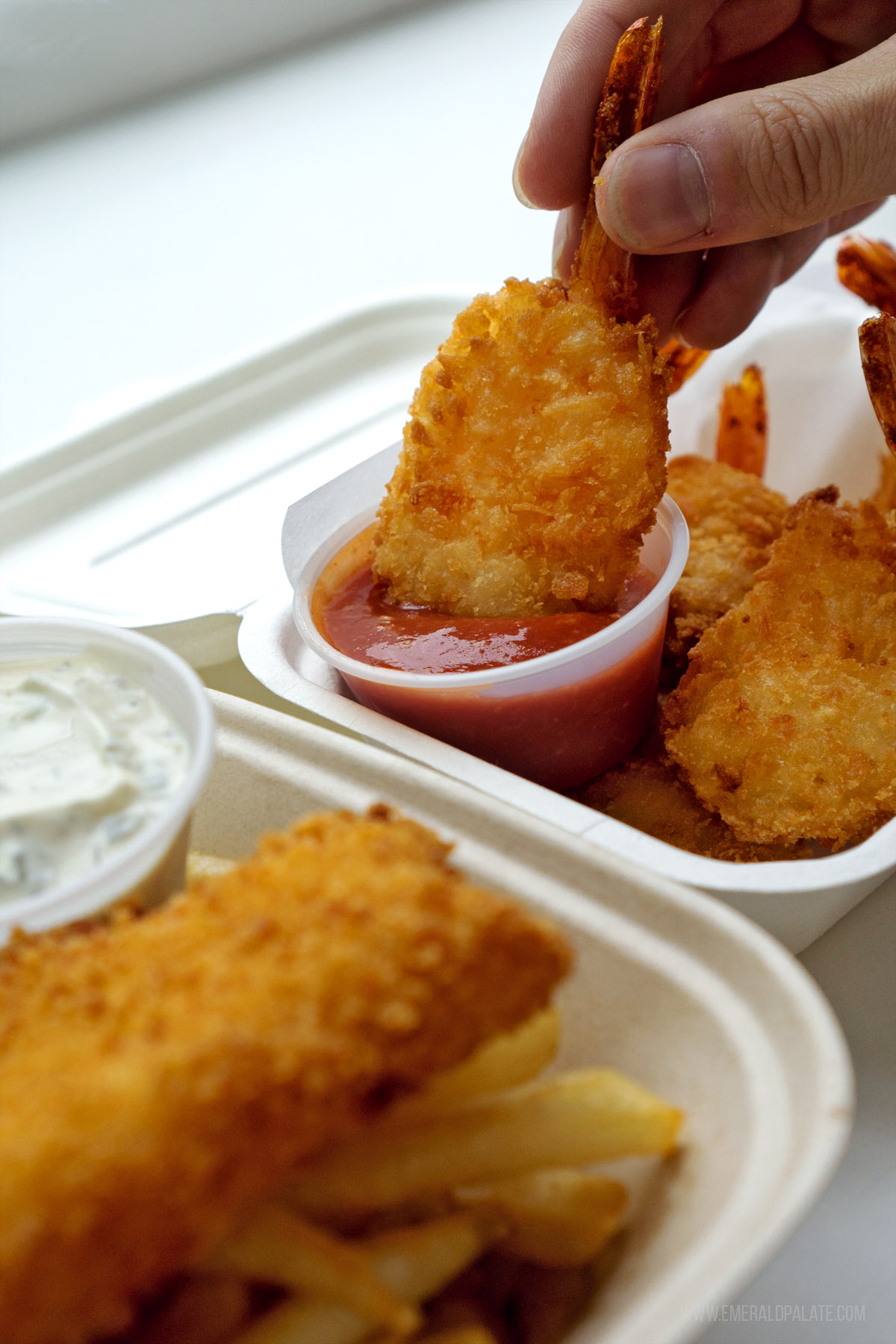 person dunking fried shrimp into cocktail sauce