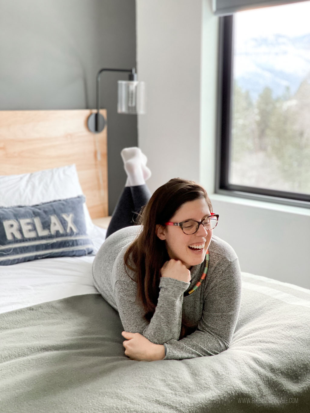 woman laughing on a bed of a cabin in Winthrop WA with views of trees out the window