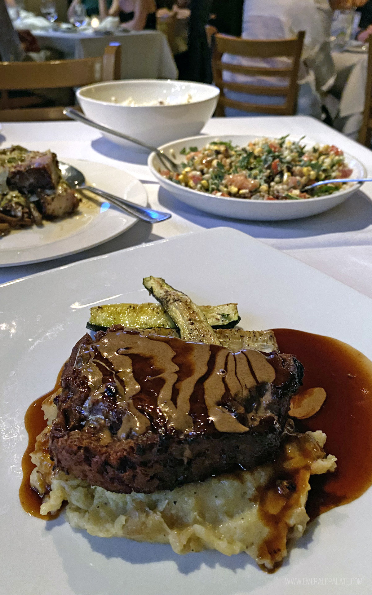 table with meatloaf over mashed potatoes, chopped salad, and a pastrami dish