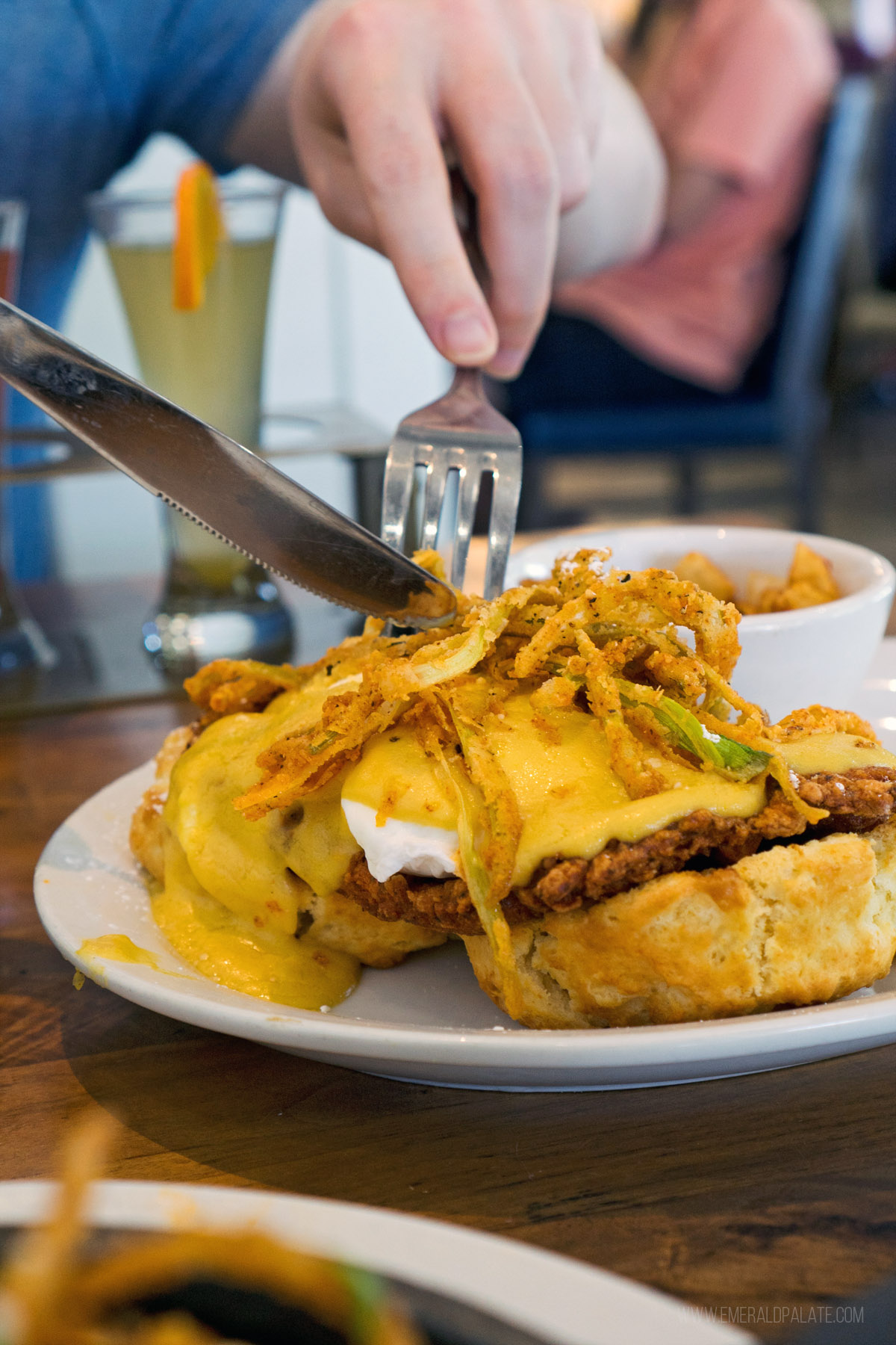 person cutting into Benedict with fried chicken