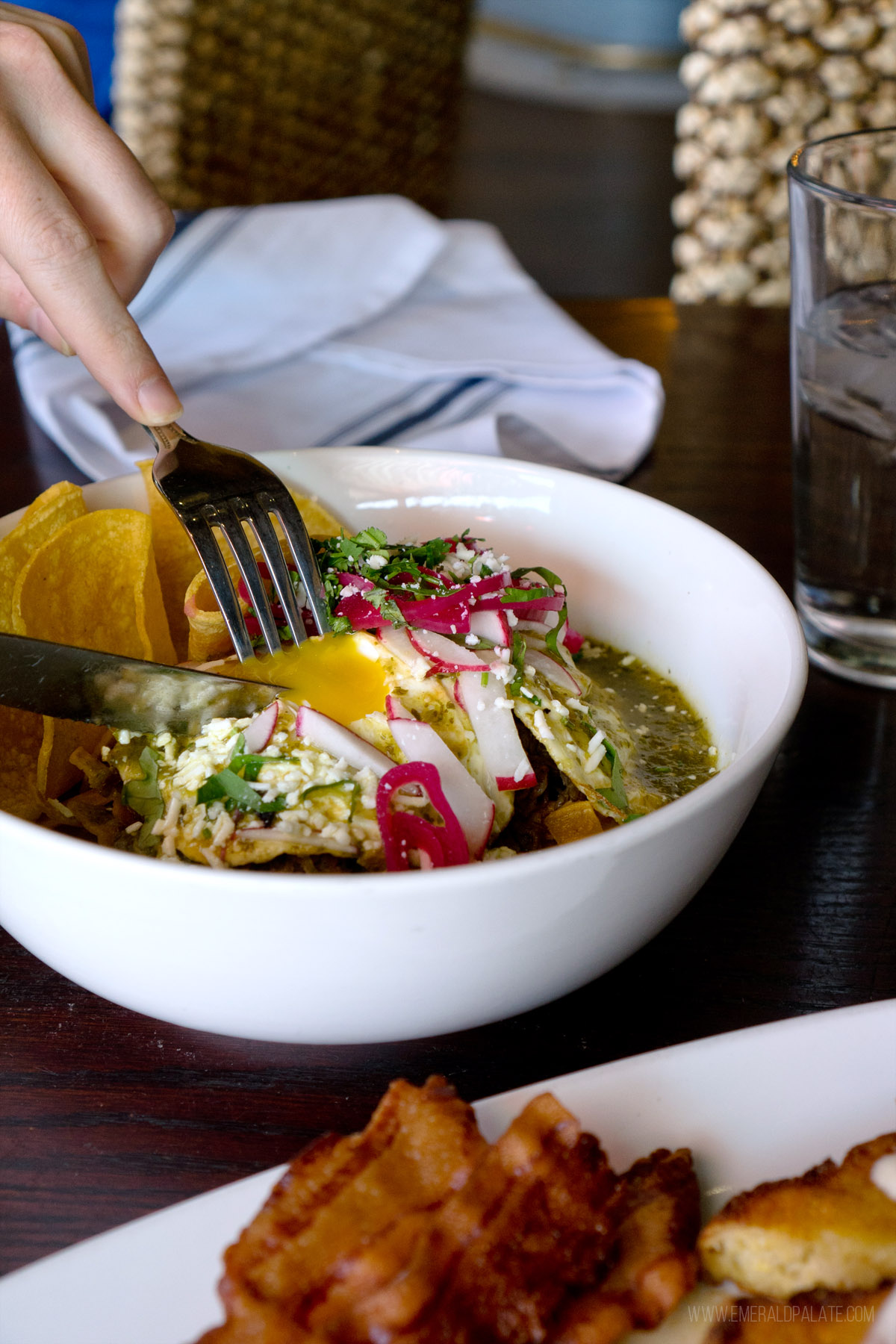 person breaking into an egg yolk of a chilaquiles breakfast dish