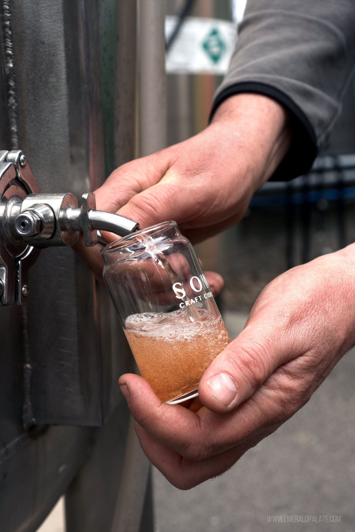 person pouring cider in a tasting glass out of a barrel