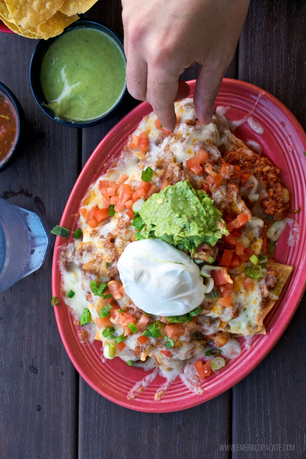 a plate of fully loaded nachos topped with sour cream and guacamole