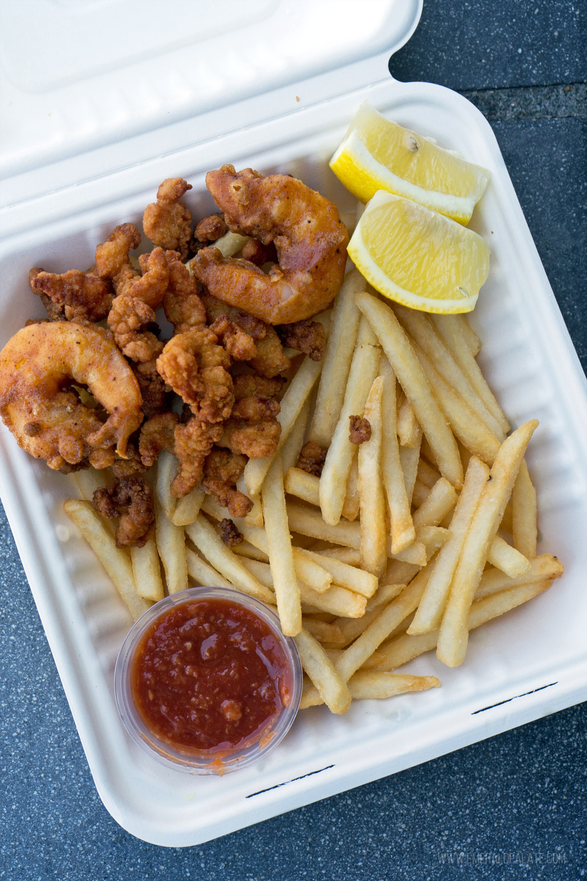 Fried shrimp, clam strips, and fries in a takeout container