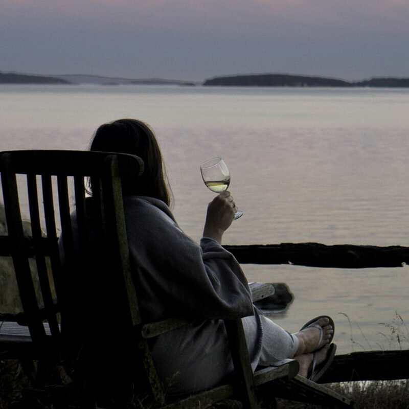 woman enjoying wine at sunset looking out on the water from one of the best Pacific Northwest cabins