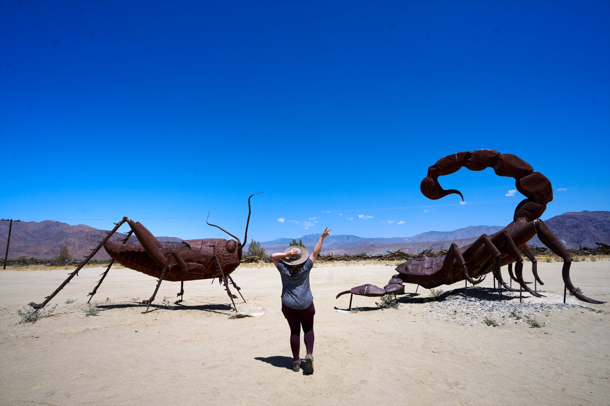 woman giving the peace sign in front of huge insect sculptures, accessible via one of the many San Diego road trips