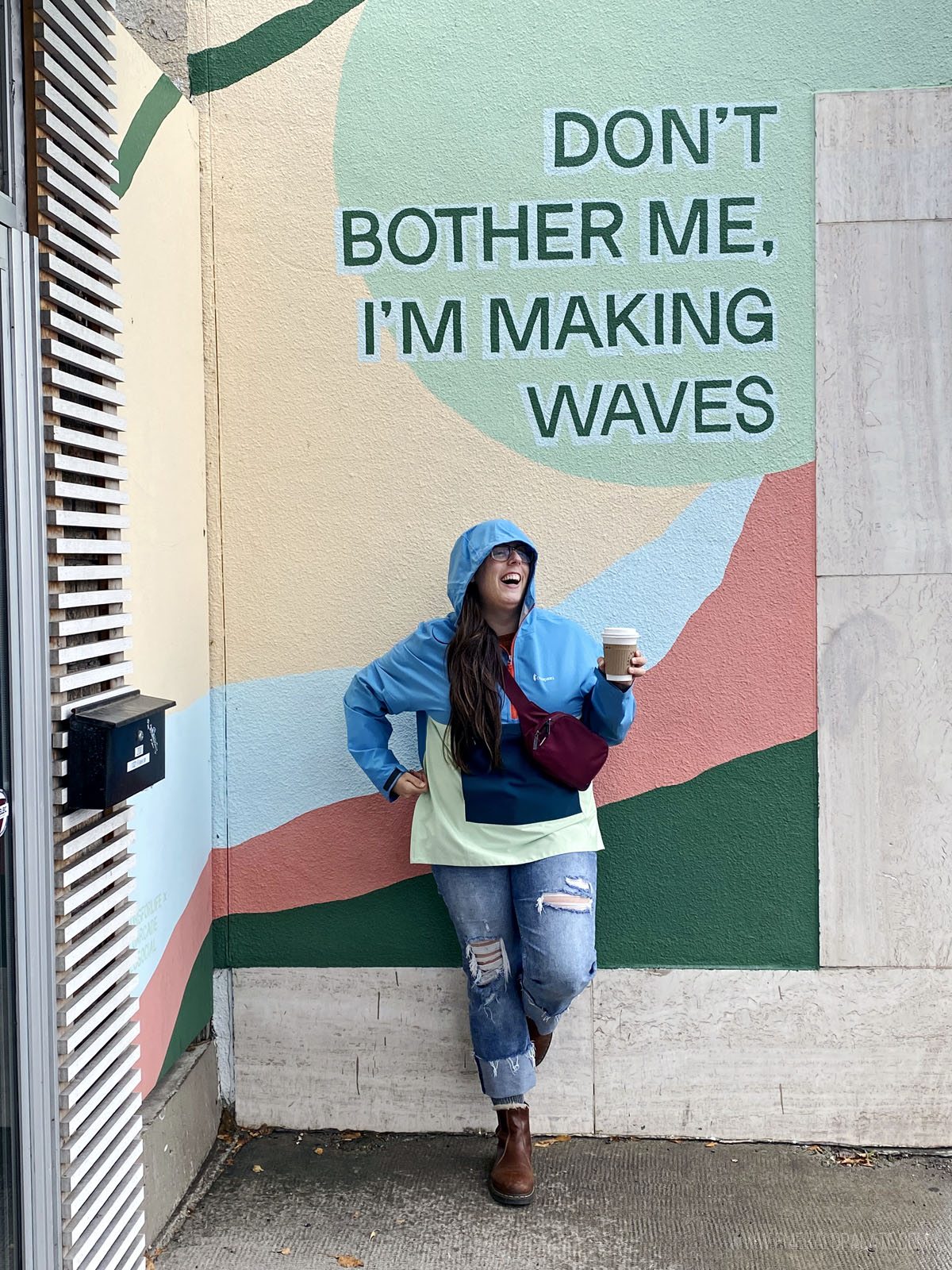 woman laughing with coffee in front of a mural during a weekend in Calgary