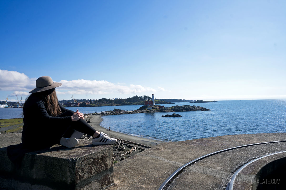 woman sitting on a fort in front of a lighthouse, one of the most unique things to do in Victoria BC