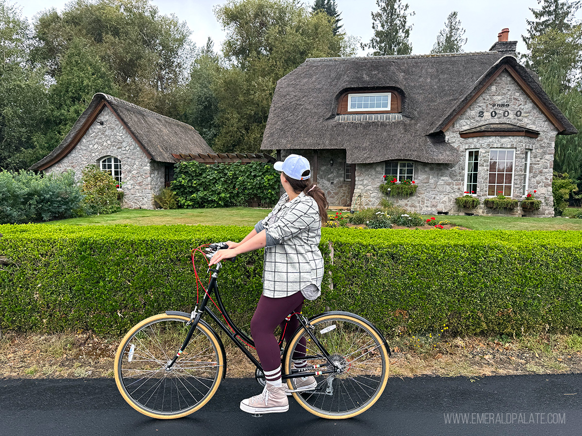 woman on a bike stopping to take in the views of an old world looking English cottage