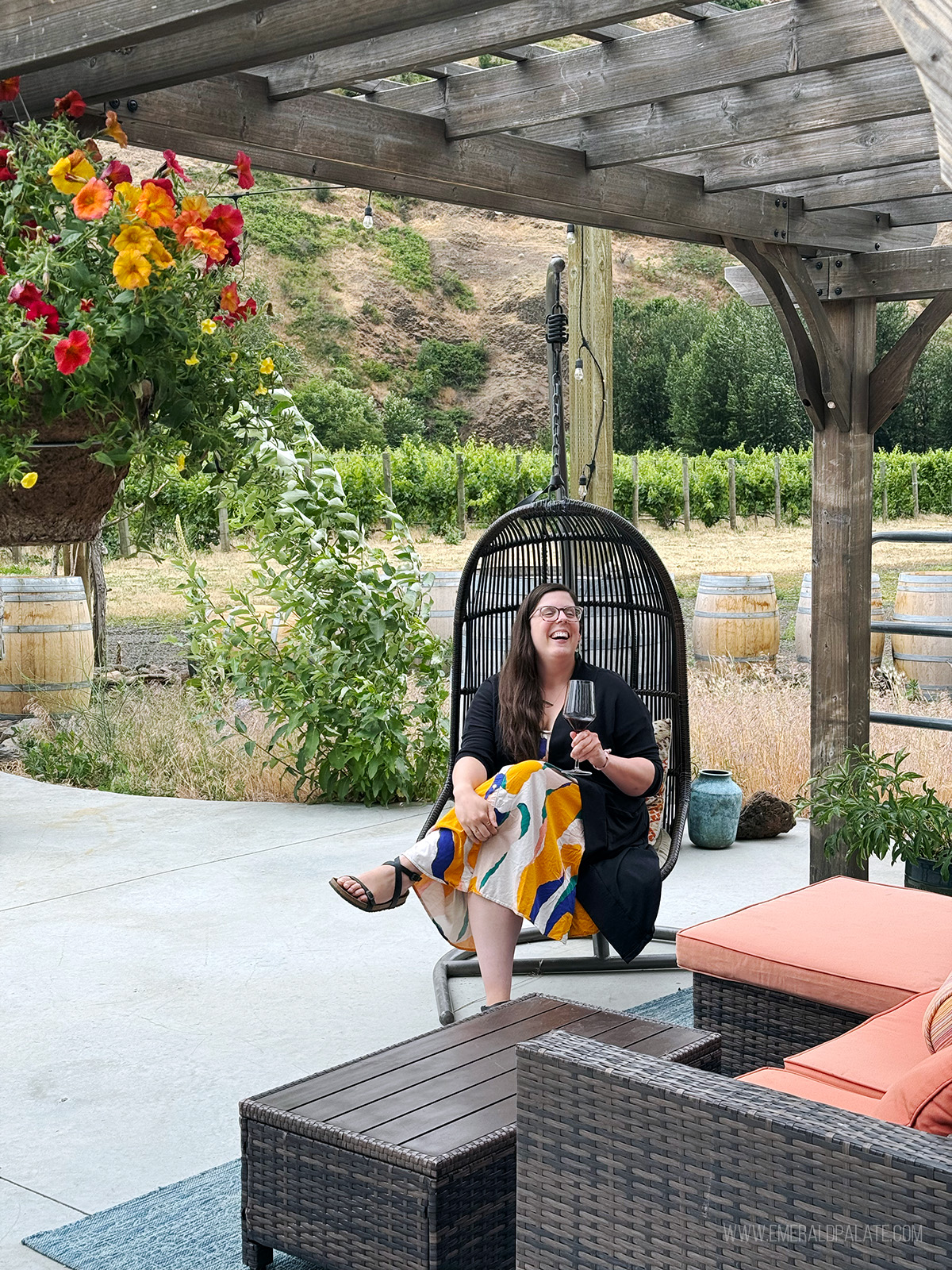 woman laughing in an egg chair on a patio while enjoying wine