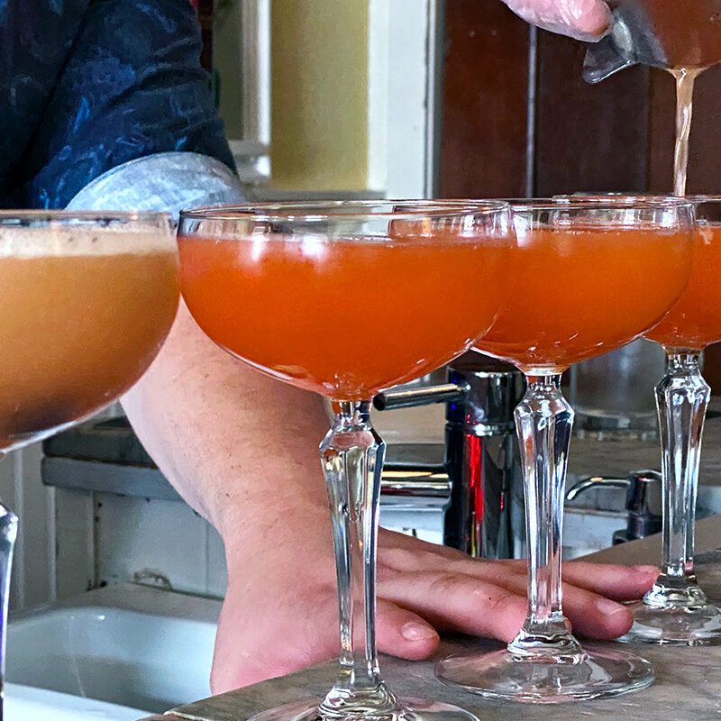 person pouring drinks into a row of the best cocktails in Seattle
