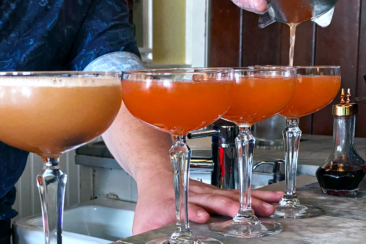 person pouring drinks into a row of the best cocktails in Seattle
