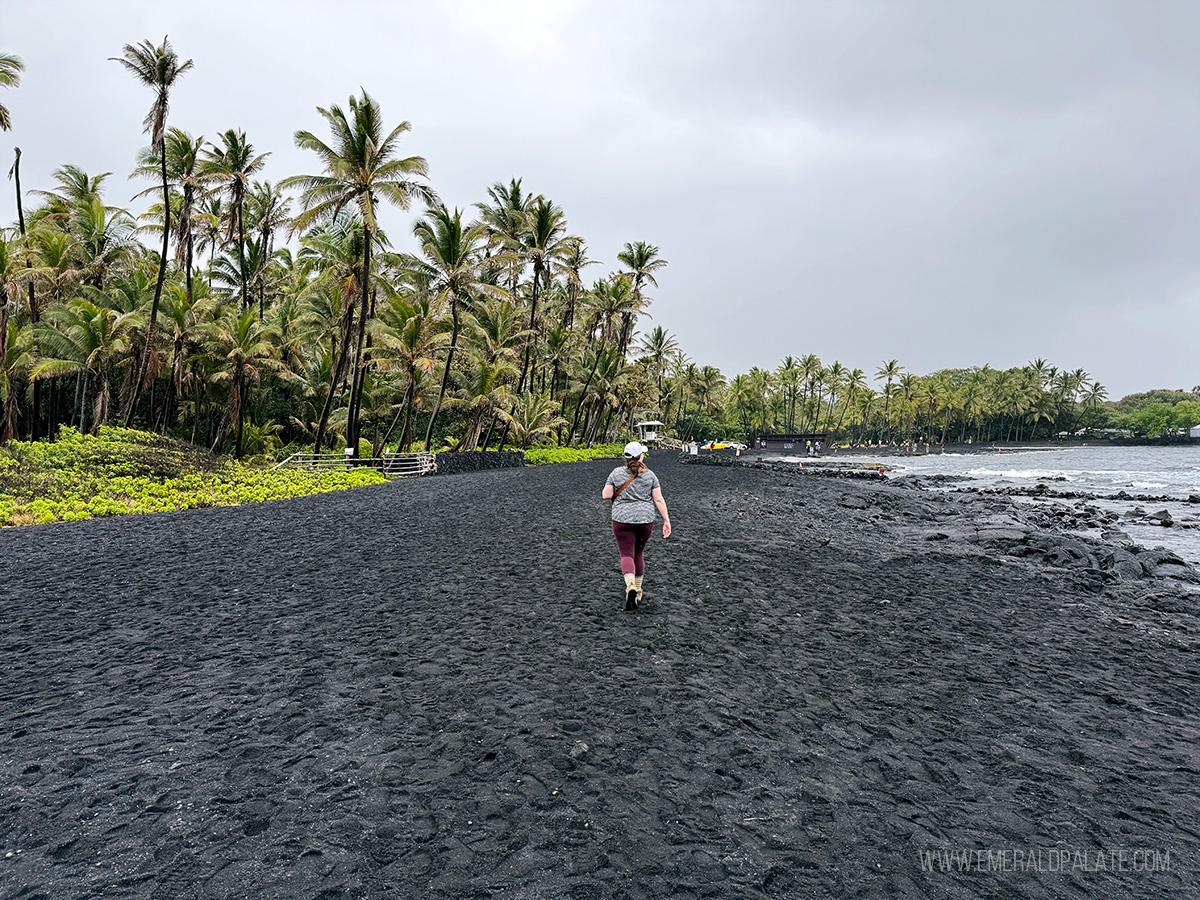 person walking along a black sand beach on the Big Island in Hawaii